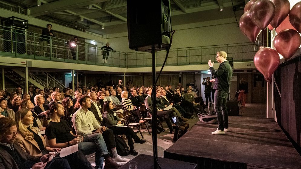 David on stage with rose-gold balloons in front of a seated audience